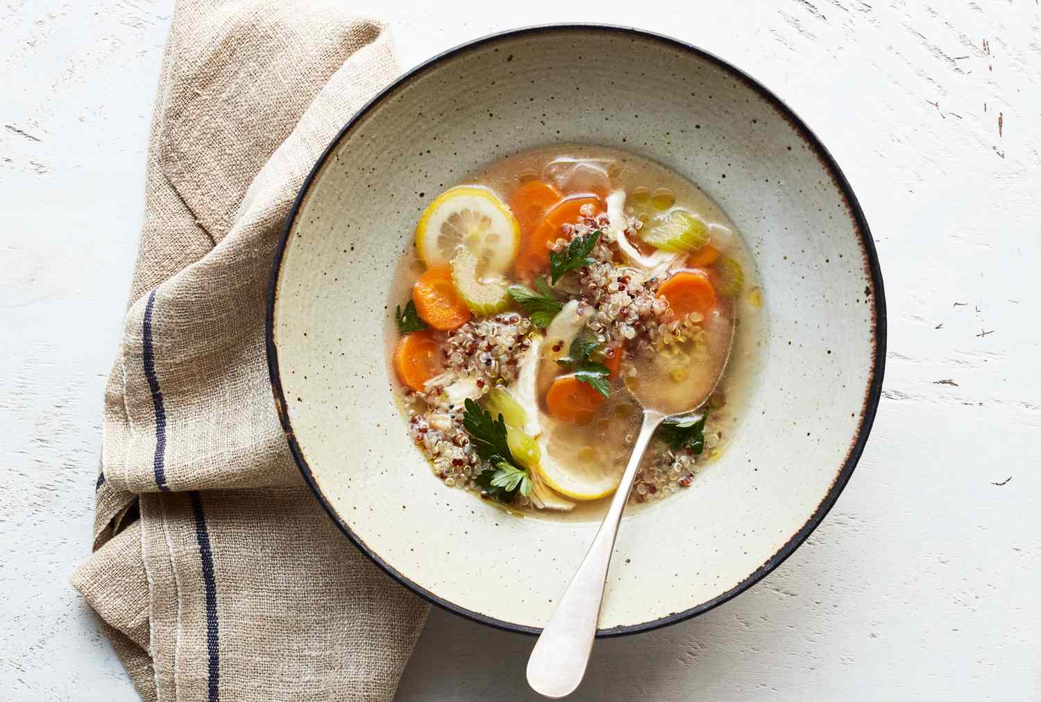 A bowl of quinoa vegetable soup with a spoon on a table