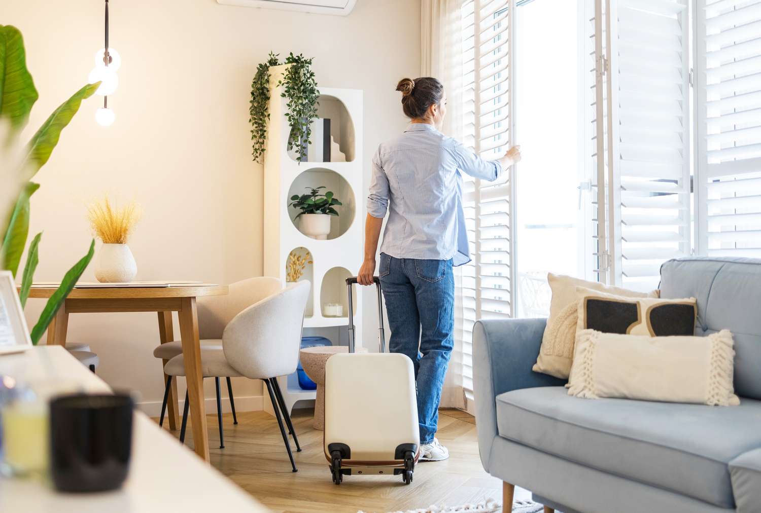A person standing near a window with a suitcase in a living room setting
