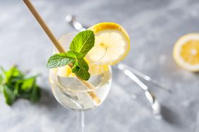 A cocktail garnished with a lemon slice and fresh mint in a glass with a straw