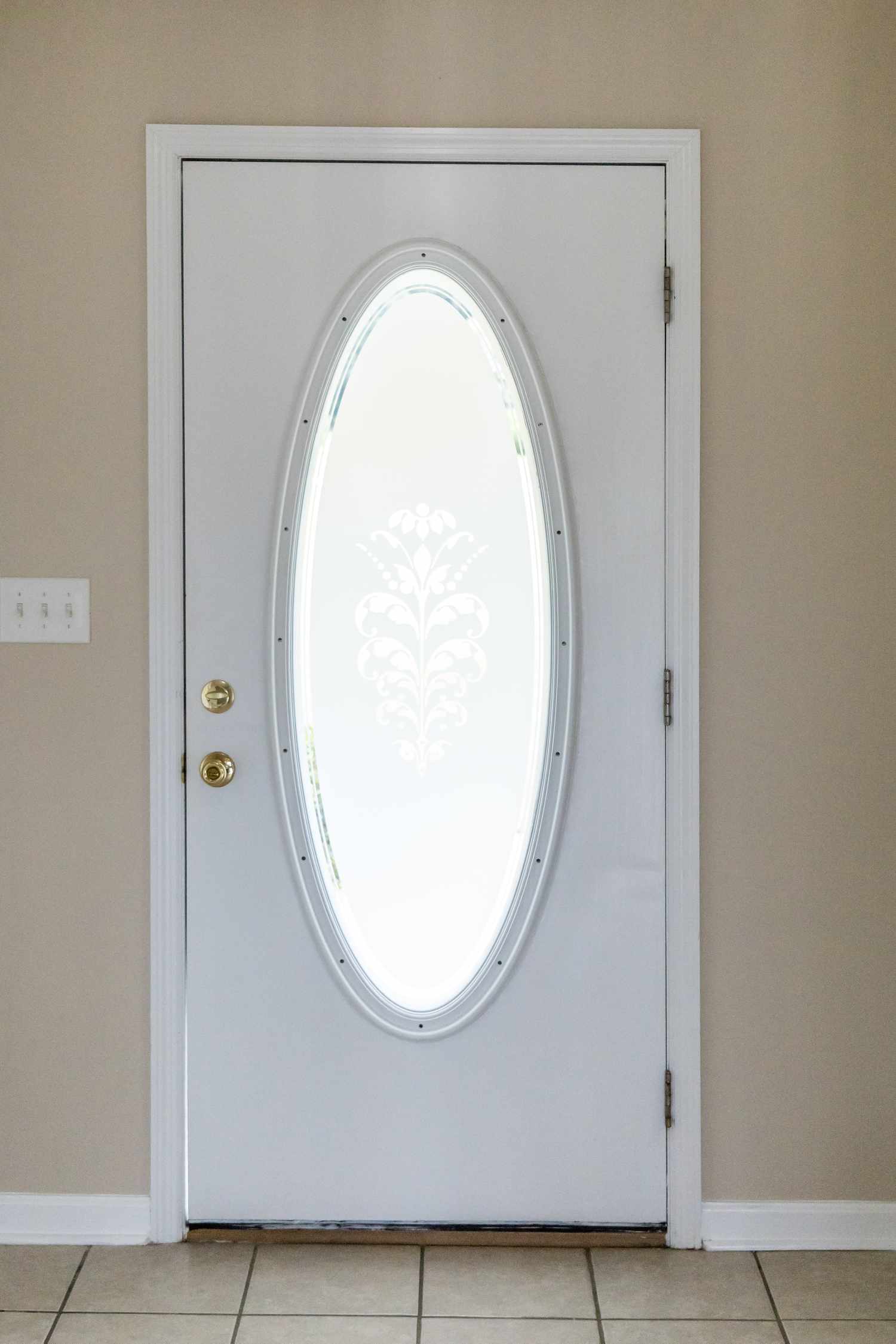 A white door with an oval glass panel in its center featuring a decorative pattern