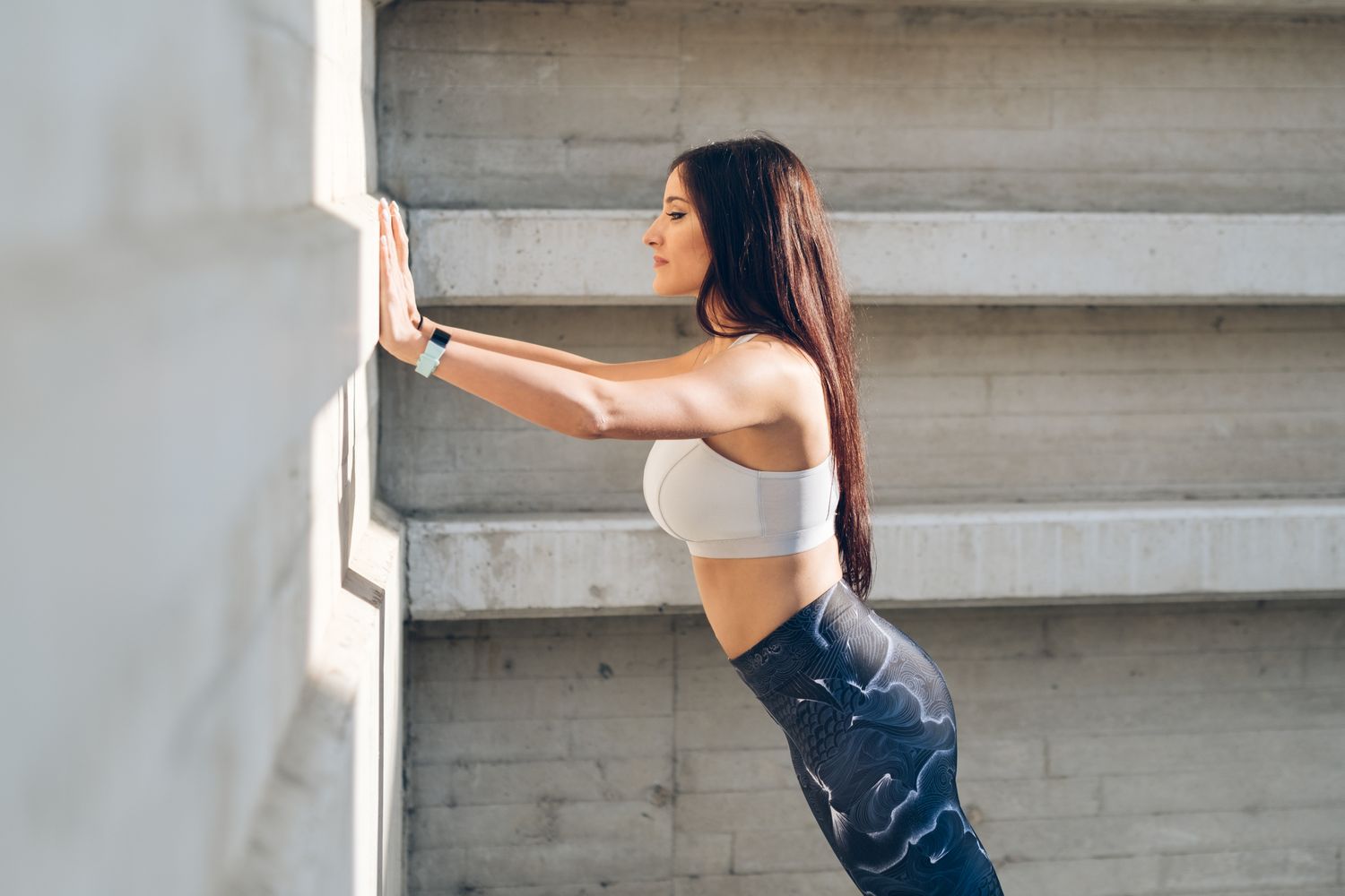 A woman exercising by pressing against a concrete wall in a modern outdoor setting