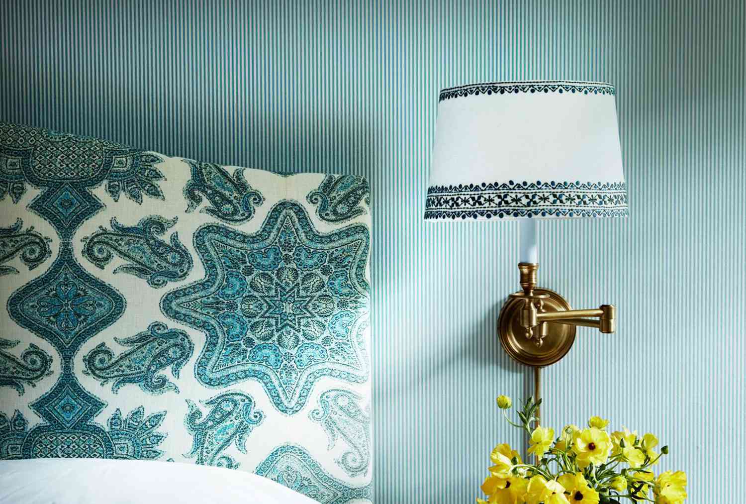 Blue striped wallpaper with golden wall sconce and paisley headboard