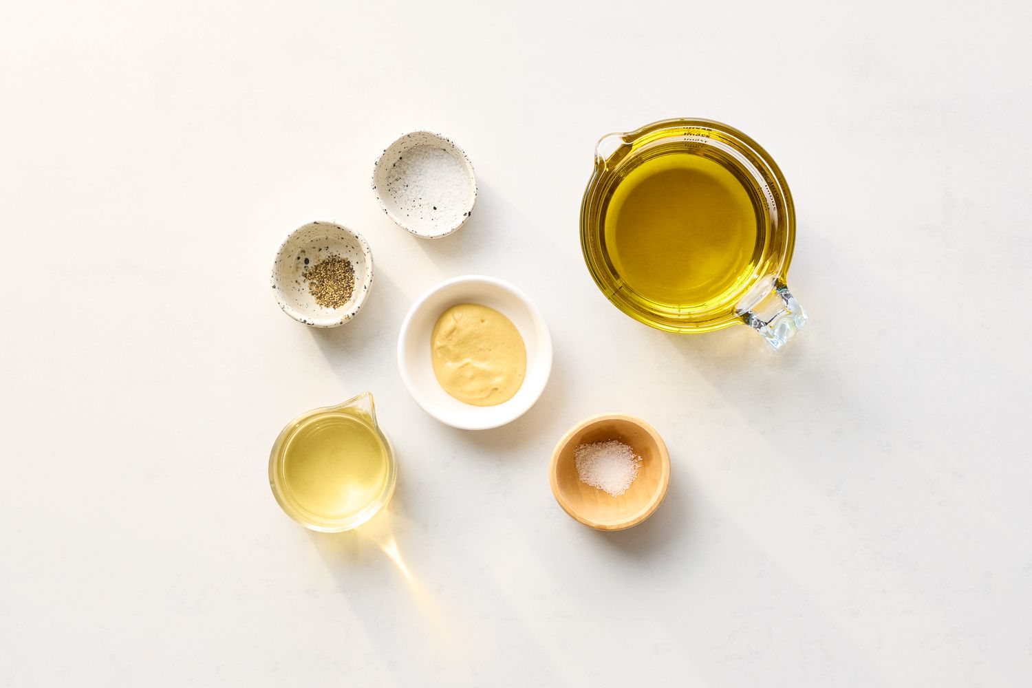 Ingredients arranged for a vinaigrette including olive oil vinegar salt pepper and mustard each in separate containers