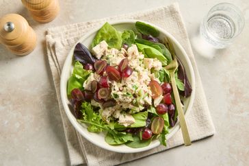 A bowl of chicken salad with mixed greens and grape halves