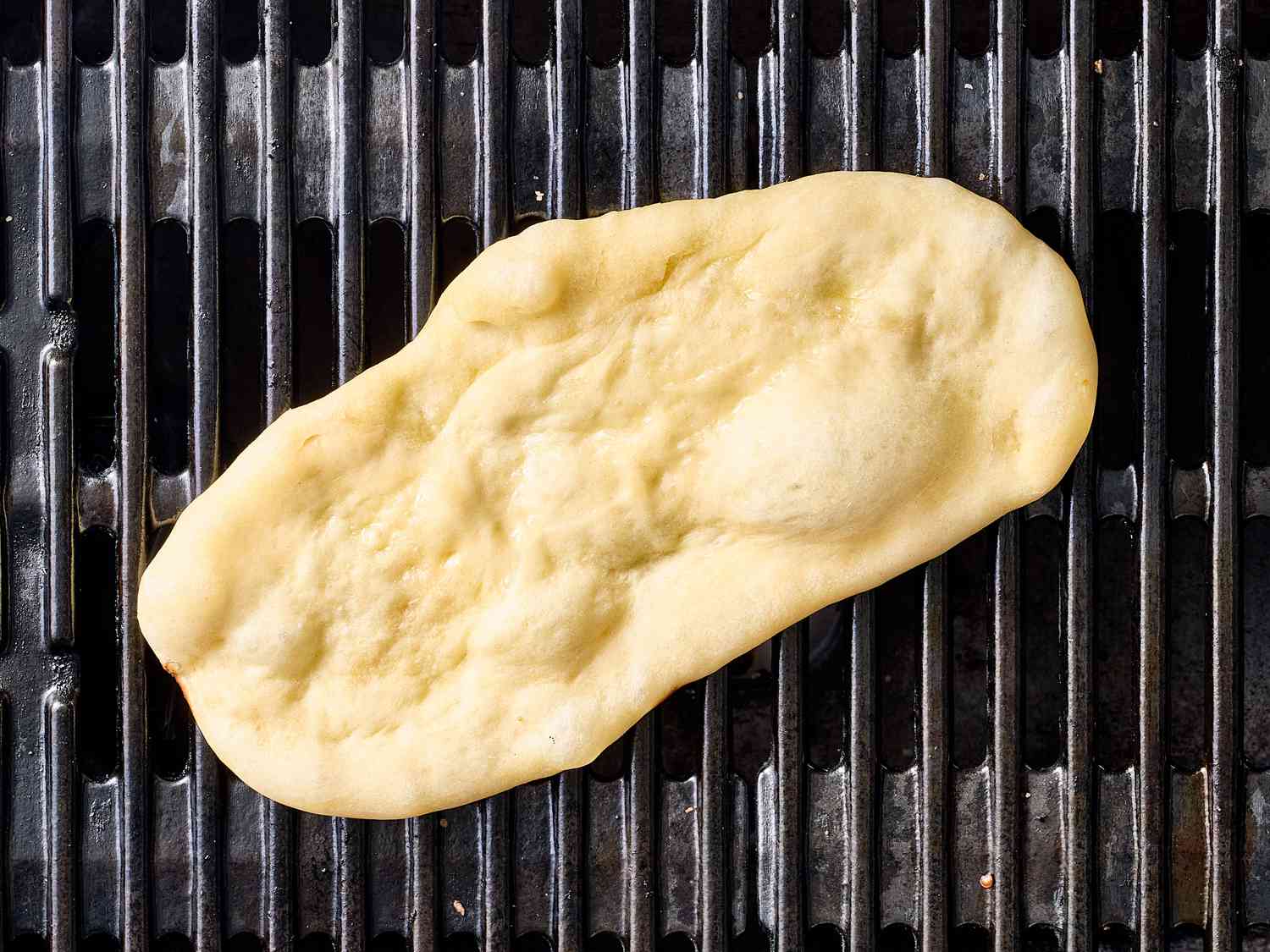 Unbaked pizza dough placed on a grill