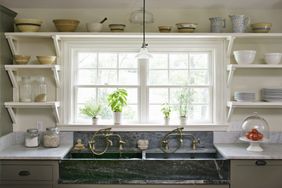 A kitchen sink with double basins under a window surrounded by shelves holding dishes and jars