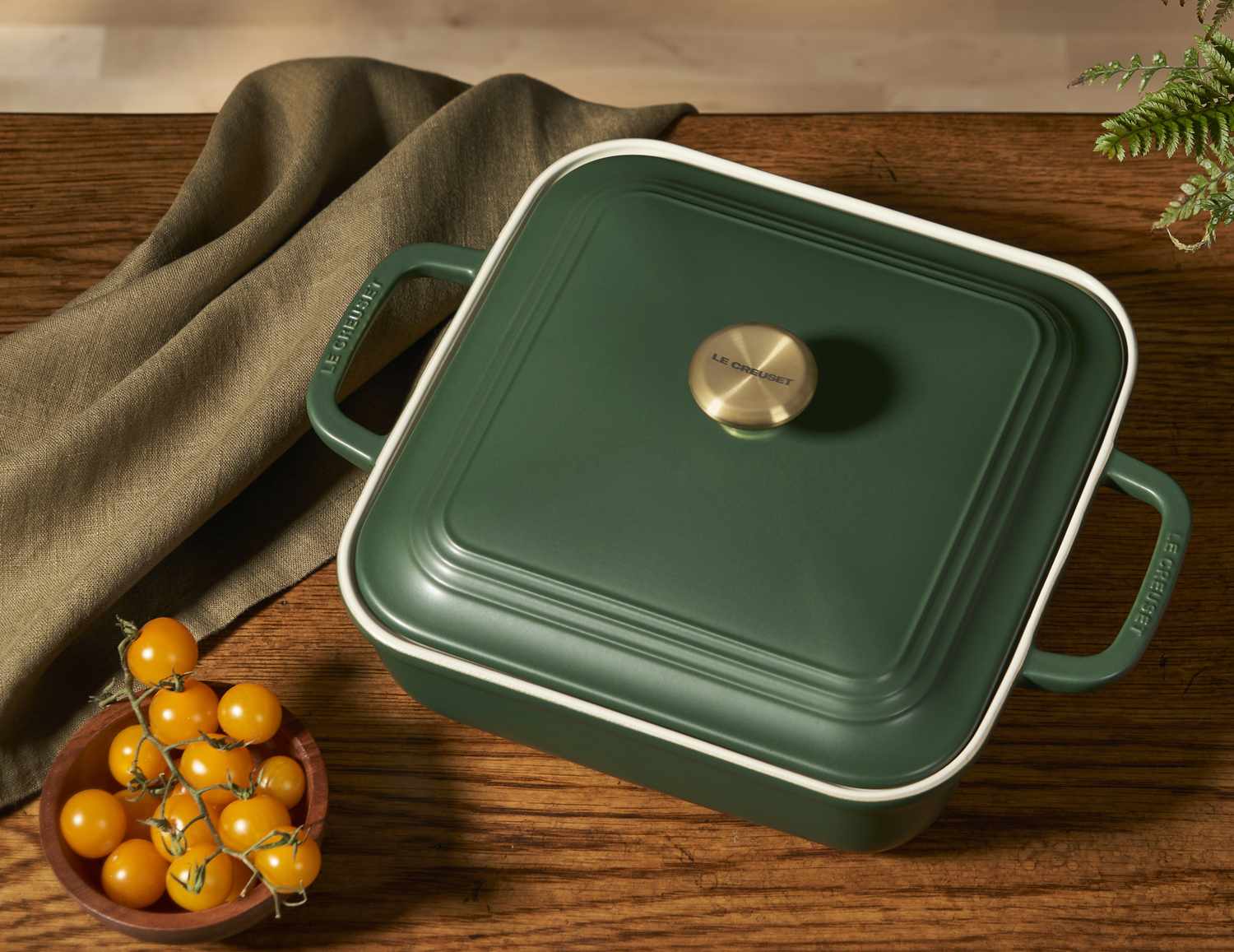 Square baking dish with lid on a wooden table next to a bowl of cherry tomatoes