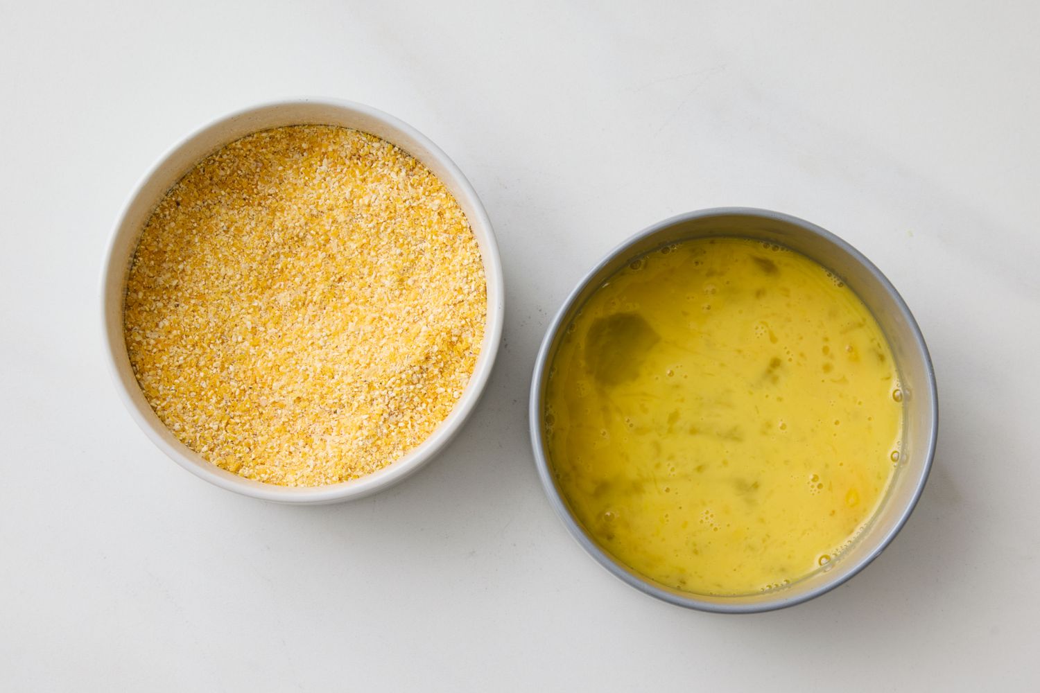 Two bowls one containing cornmeal and the other a mixture of beaten eggs