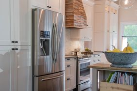 Modern kitchen with stainless steel appliances a wooden range hood and fruit in a bowl on a counter
