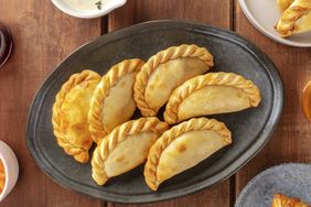 A serving plate with six empanadas placed on a table, side dishes partially visible around