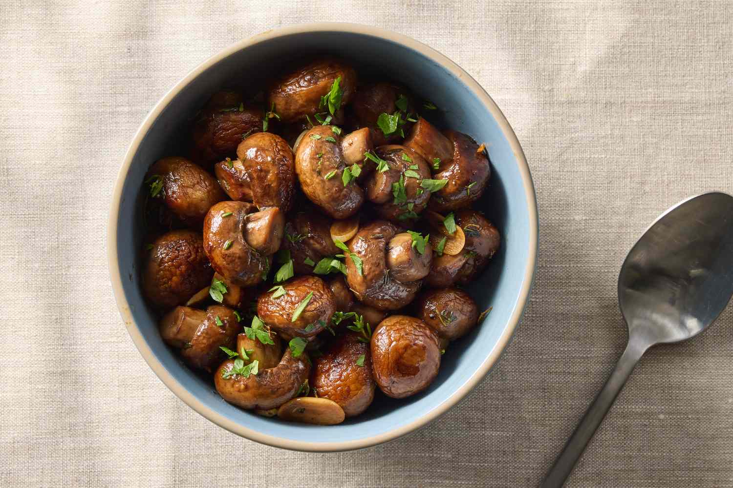 Bowl of sauted mushrooms garnished with herbs next to a spoon