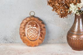 Copper cake mold next to a copper vase on a concrete background.