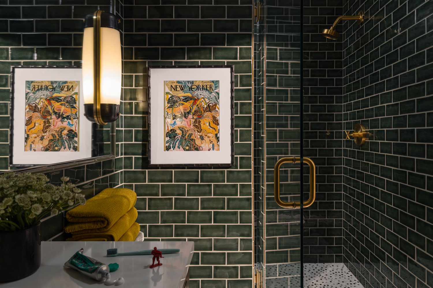 A bathroom tiled completely in emerald green subway tiles with brass hardware accents
