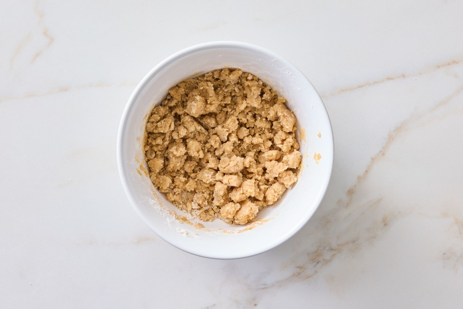 A bowl with a mixture of crumbly dough on a light surface