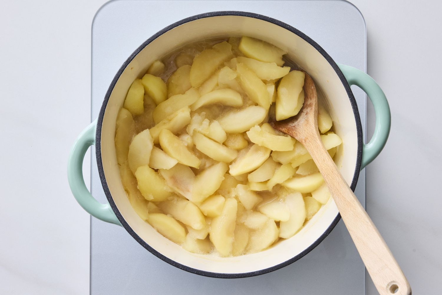 A pot of sliced apples being cooked with a wooden spoon