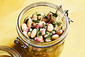 A jar filled with bean salad including white beans chopped herbs and diced red onions