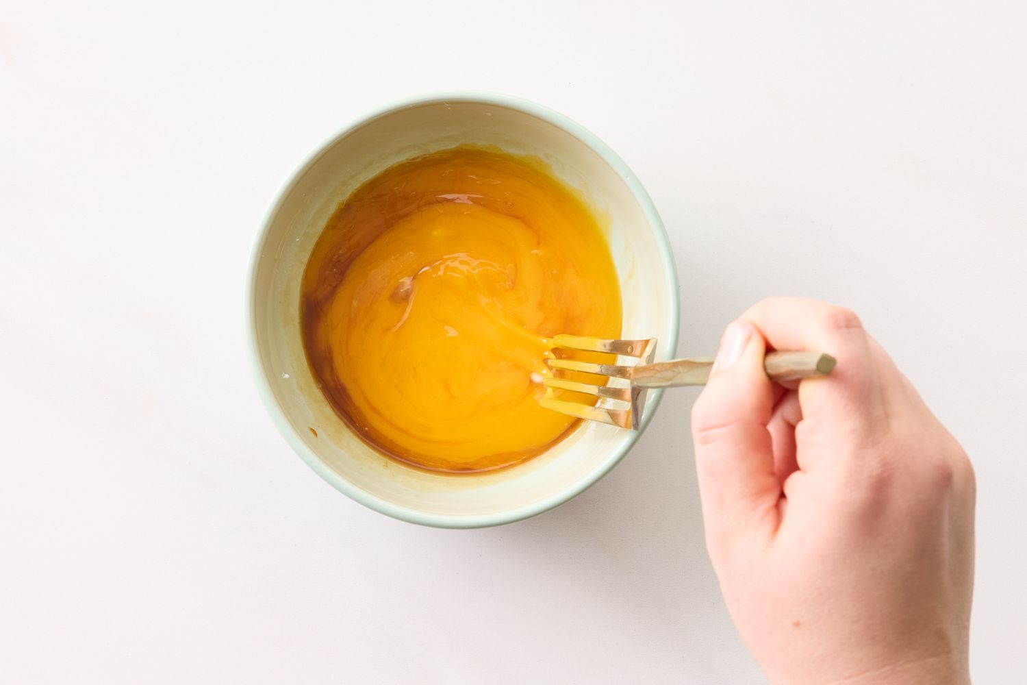 A hand mixing egg yolks in a bowl using a fork
