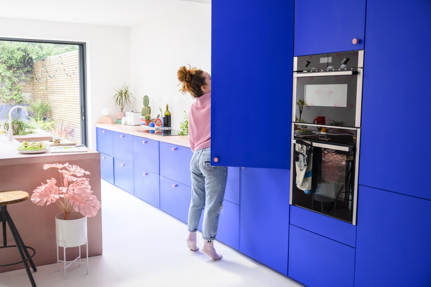 A person reaching into a kitchen cabinet in a modern kitchen with blue cabinetry