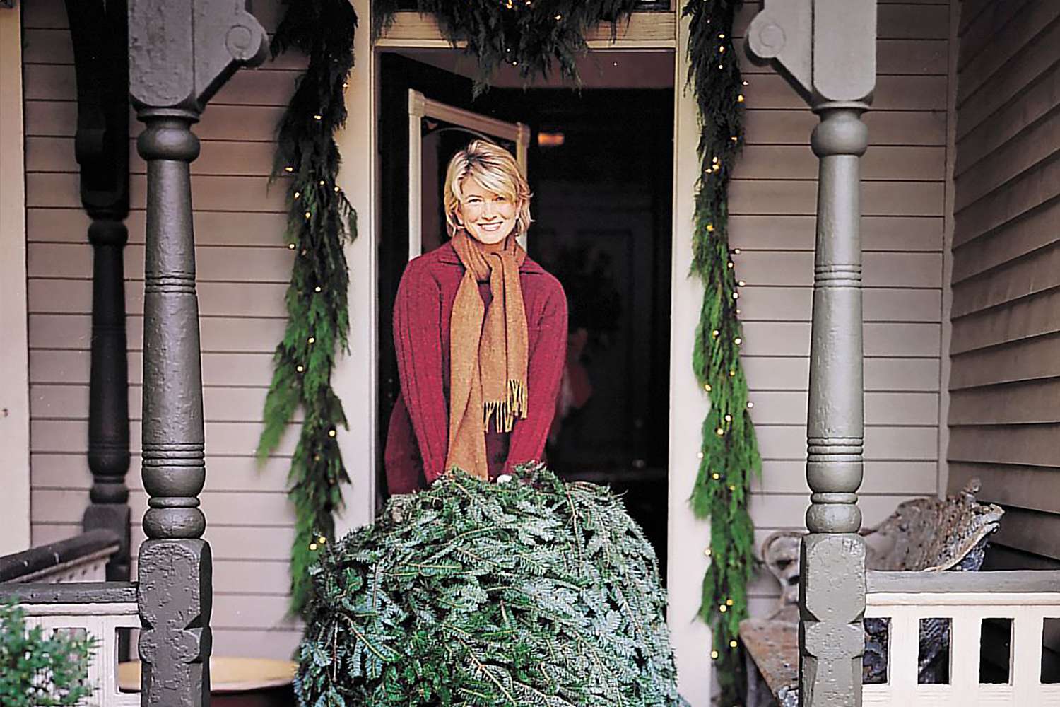 decorvow holding a Christmas tree on a front porch
