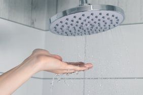 A hand checking water flow under a shower head
