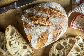 A loaf of crusty artisan bread with sliced pieces on a wooden board
