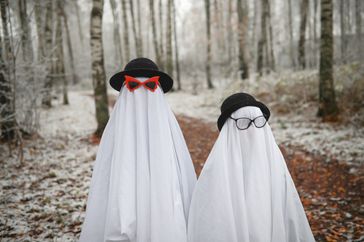 Two figures dressed as ghosts wearing hats and glasses standing on a forest path