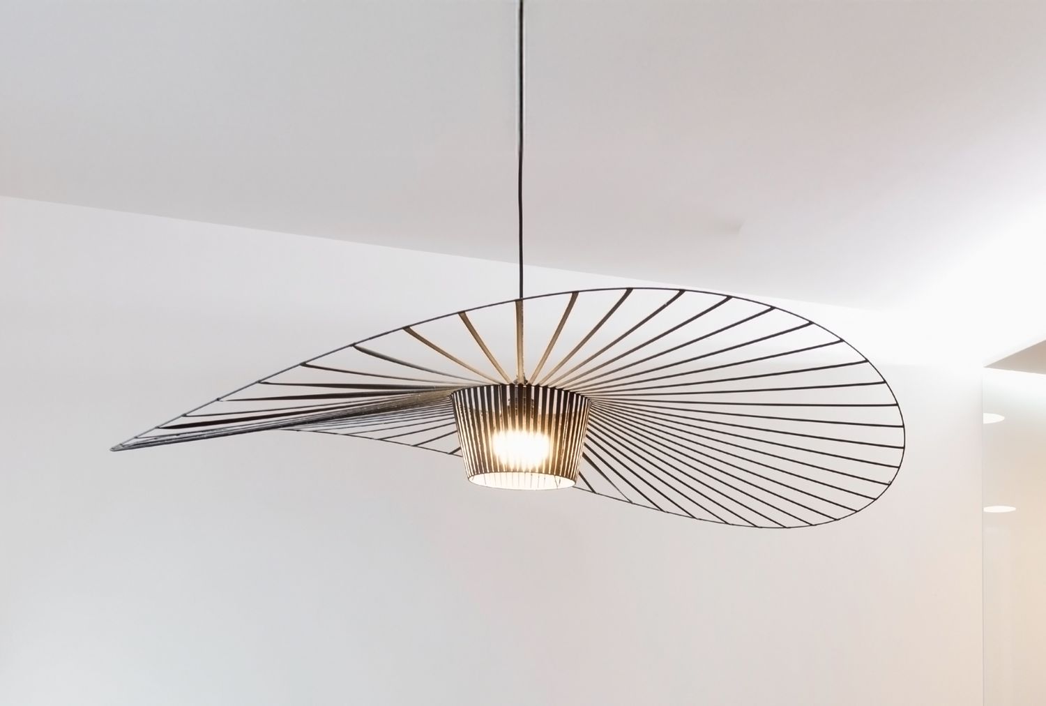 A modern ceiling light with a linear wave design suspended in a minimalist room