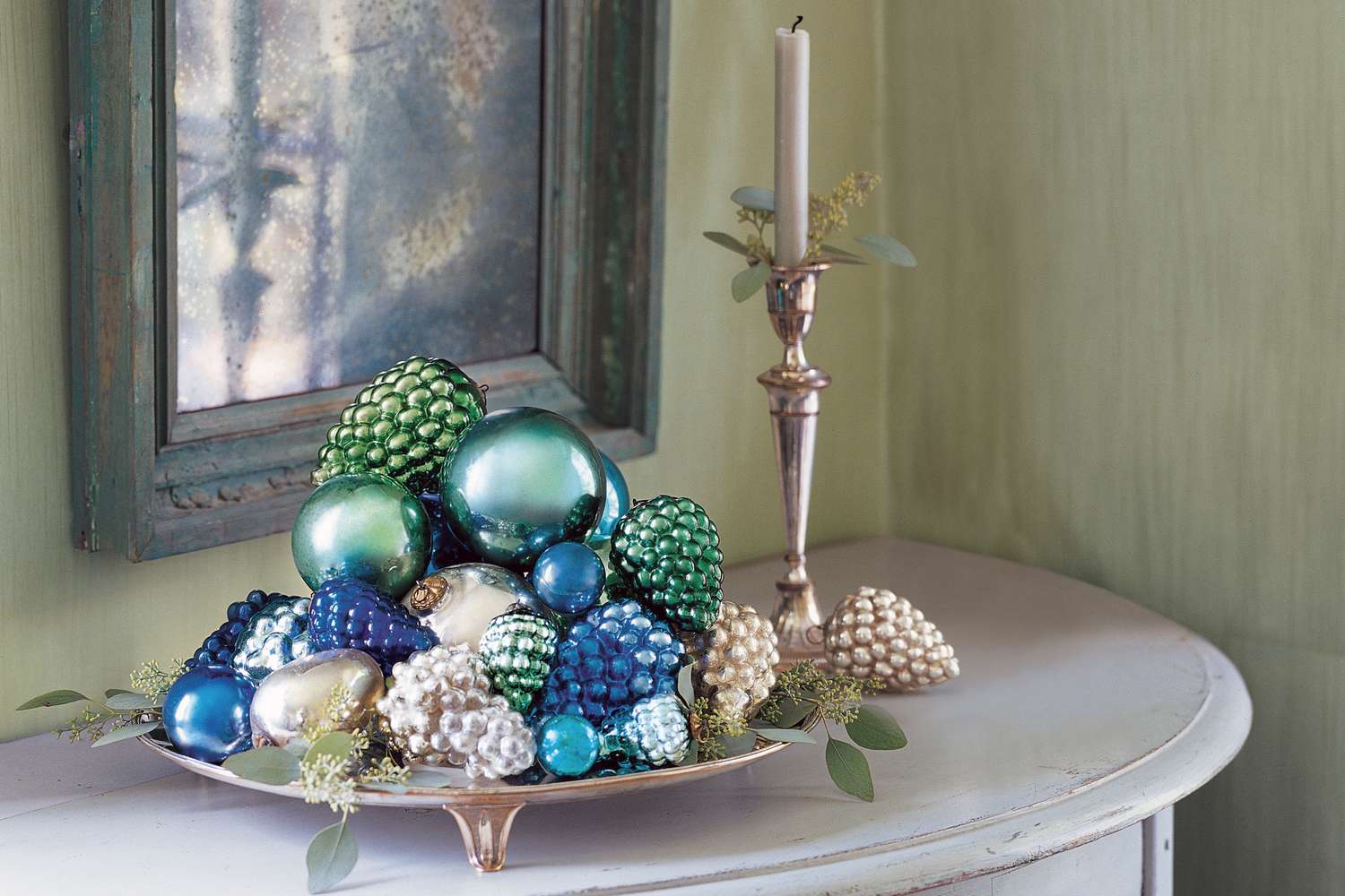 An arrangement of decorative ornaments piled on a tray next to a candle on a holder on a table