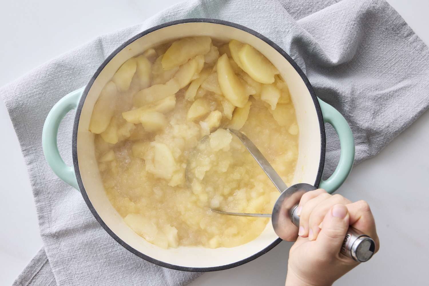 Hand mashing cooked apples in a pot for applesauce