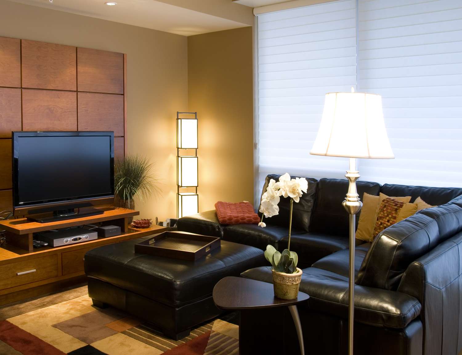 A cozy living room with a black leather sectional a television on a stand and a coffee table with a potted orchid
