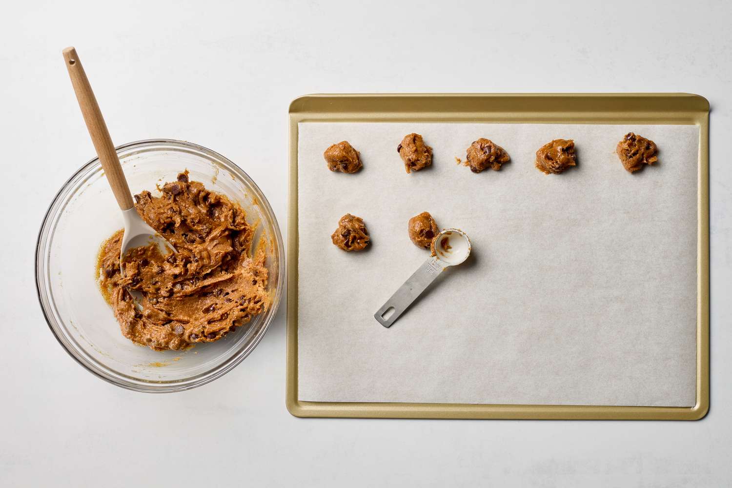 Bowl of cookie dough with a spoon and a baking tray with portioned cookie dough scoops