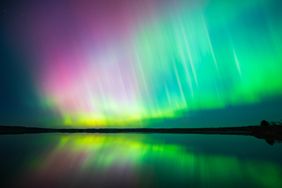 Colorful aurora borealis lights reflected on the surface of a calm lake at night