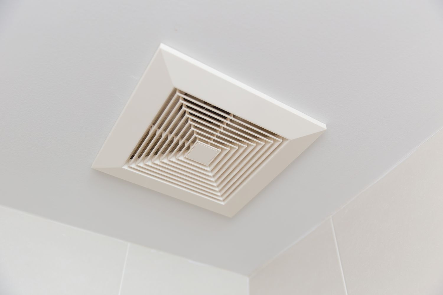 A ceilingmounted ventilation fan with a louvered grille in a room corner