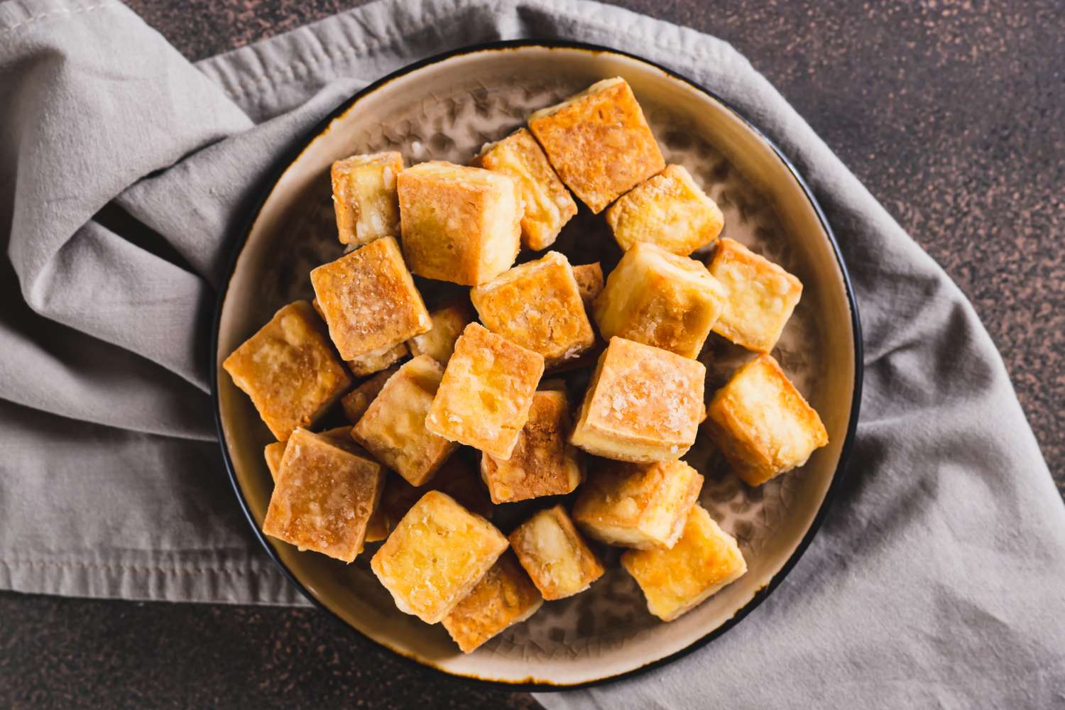 A bowl of cooked tofu cubes arranged on a table with a cloth napkin