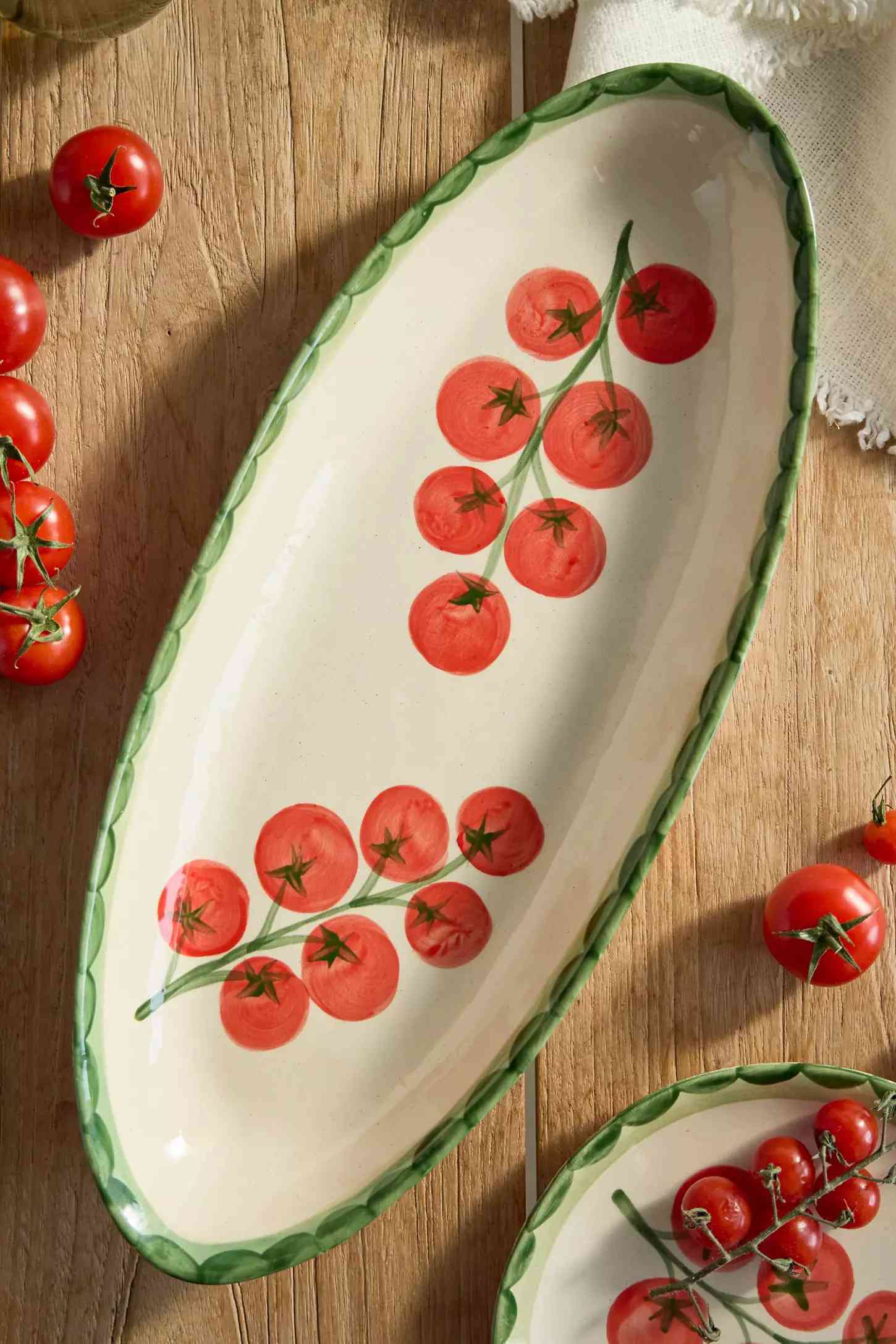 Oval ceramic dish with painted tomato vine pattern surrounded by cherry tomatoes on a wooden surface