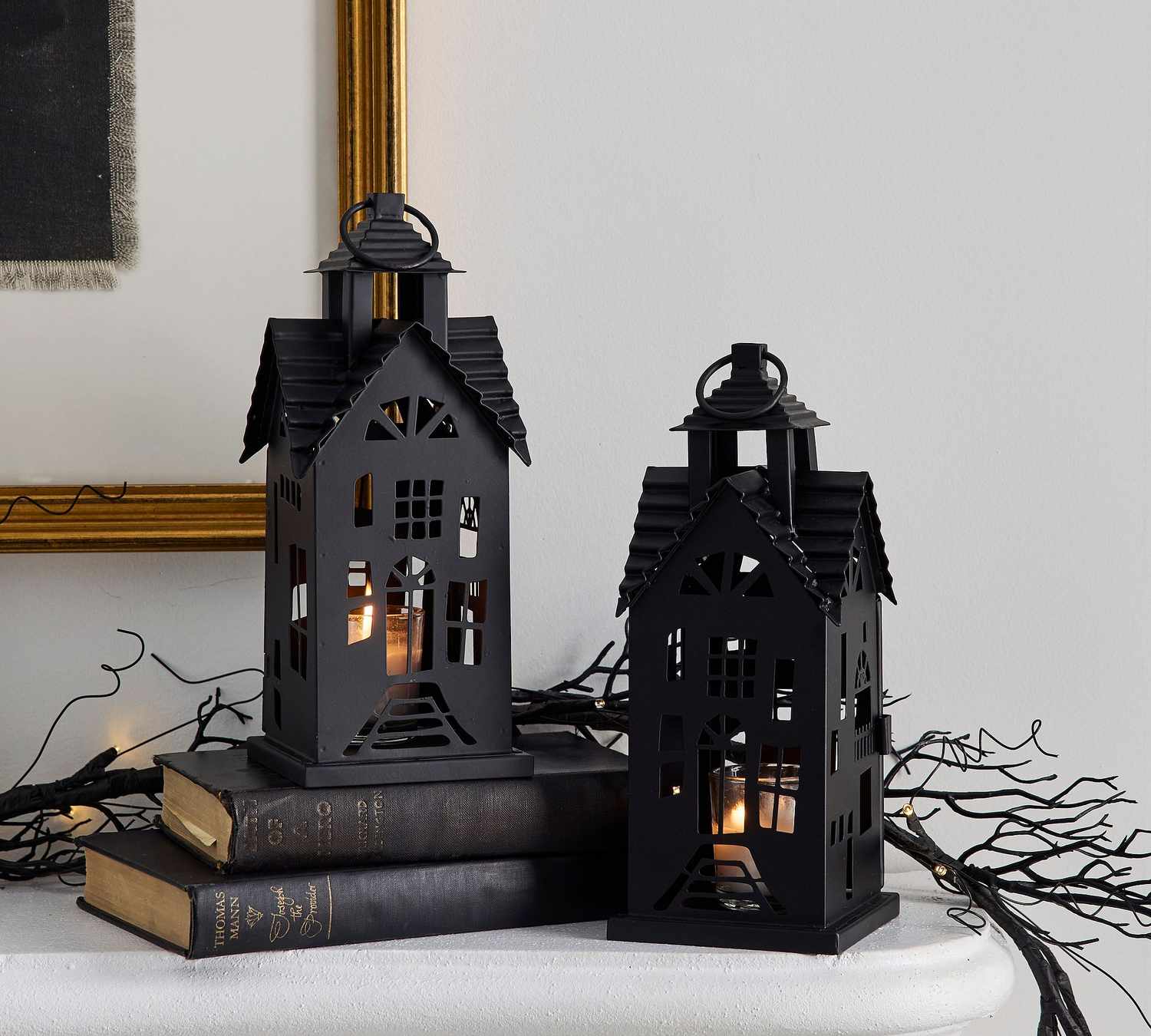 Decorative lanterns shaped like haunted houses with candles inside placed on books on a table