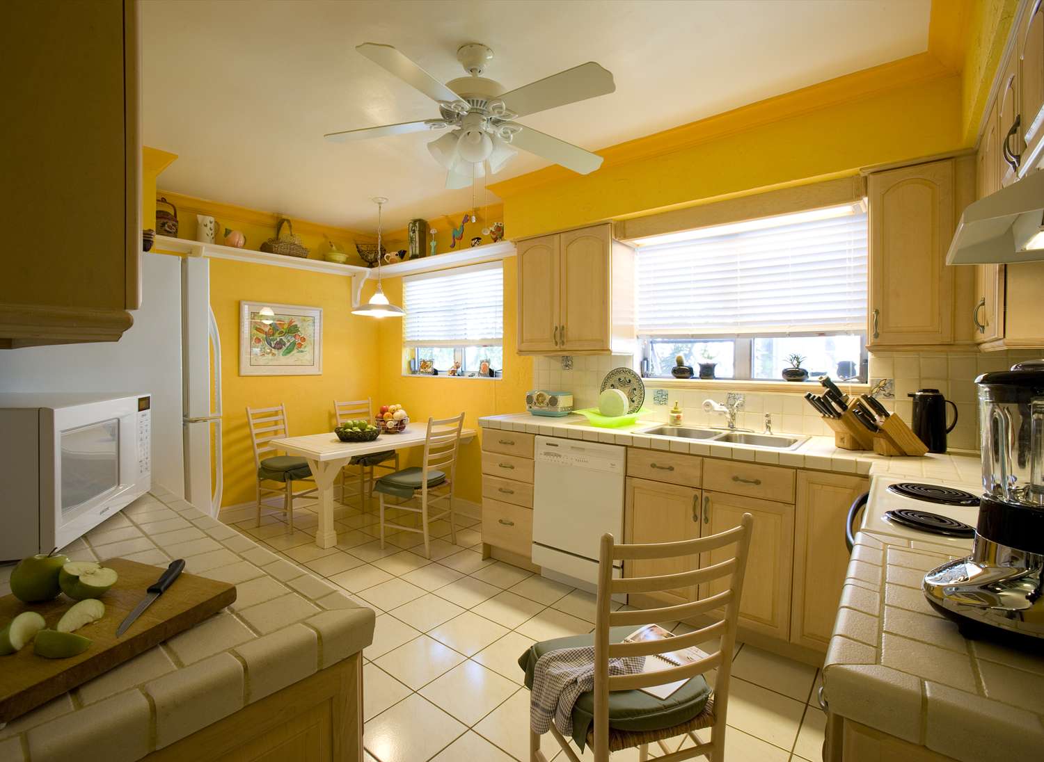 A bright kitchen with tiled countertops a dining area and a window letting in light