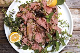 sliced lamb on a plate with herbs and lemon
