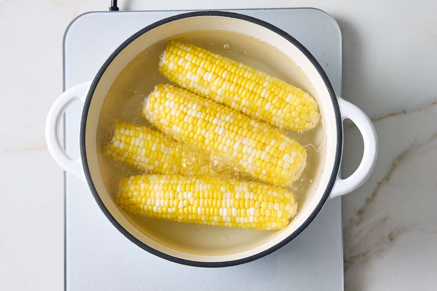 Four corn cobs boiling in water in a round pot