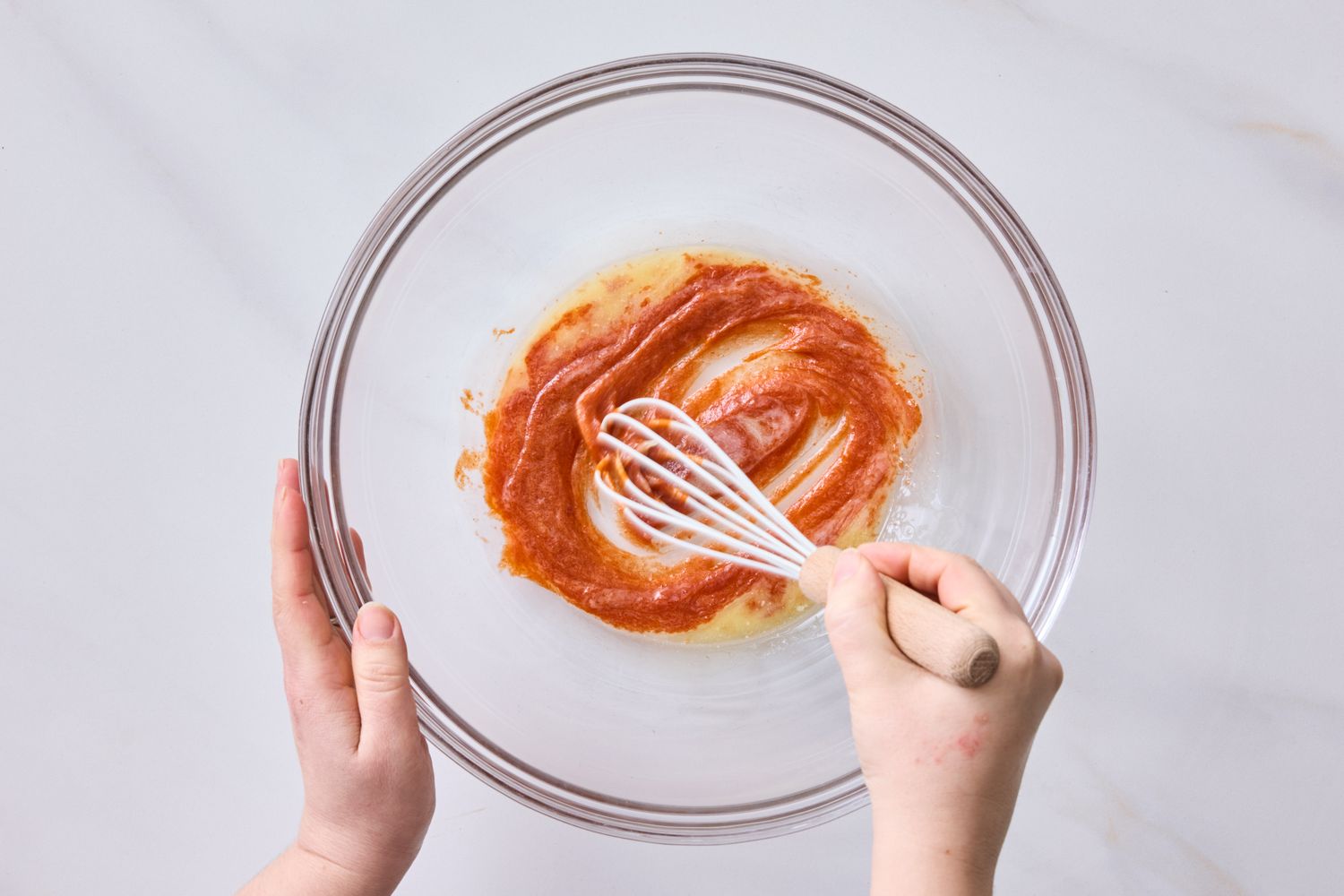 Hands whisking a red sauce in a glass bowl