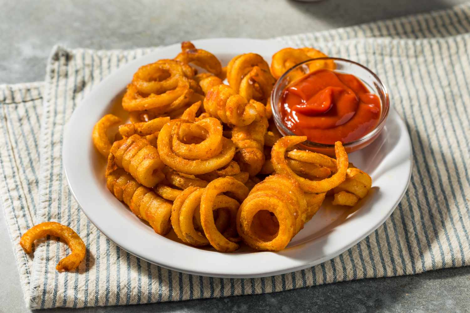 curly fries and dish of ketchup on white plate