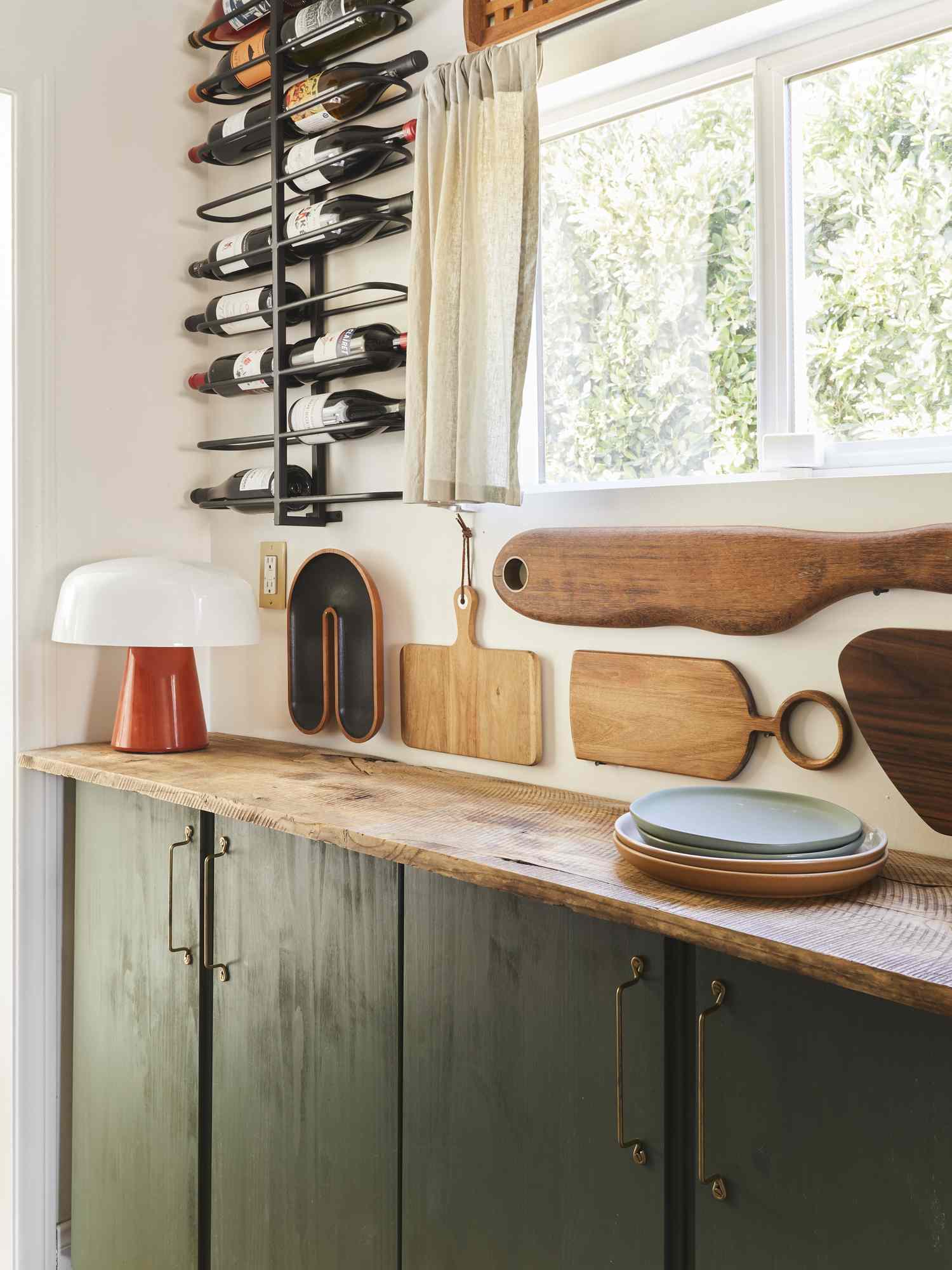 Kitchen counter with wood cutting boards on the wall stack of plates a lamp and a mounted wine rack nearby