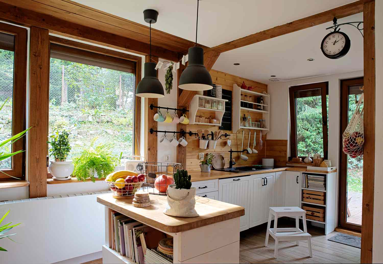 A cozy kitchen with wooden accents, a central island, and large windows overlooking greenery, shelves holding kitchen accessories