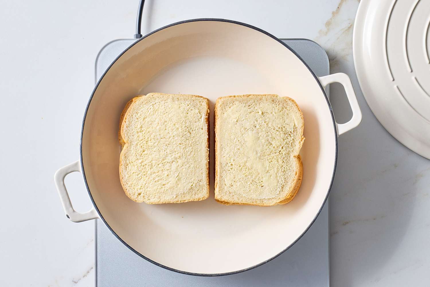 Two slices of bread with butter frying in a white skillet