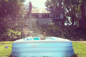 Two children playing in an inflatable pool in a backyard water splashing around them