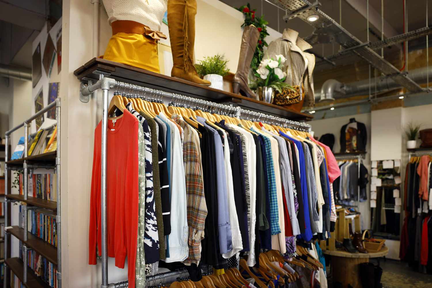 Clothing on racks in a retail store, with shelves above holding items like bags and decor