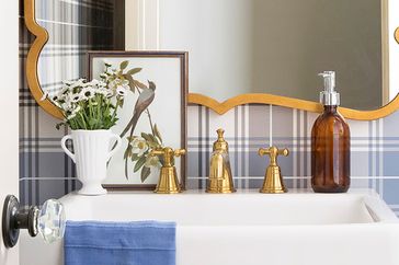 Bathroom counter with a framed bird artwork daisies in a vase golden fixtures and a soap dispenser