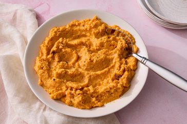 A bowl of mashed sweet potatoes with a serving fork resting on the edge