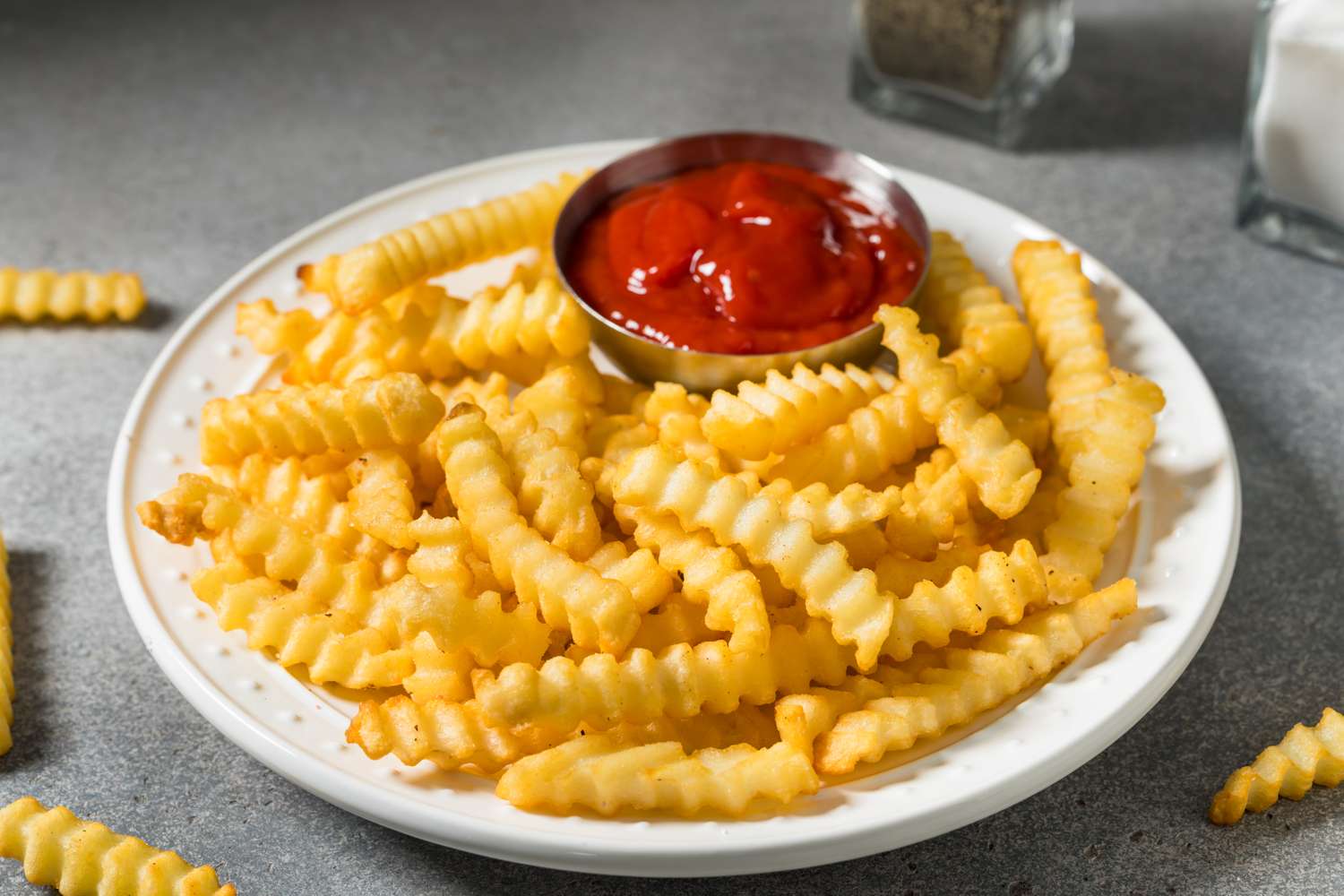crinkle cut fries on white plate with small dish of ketchup