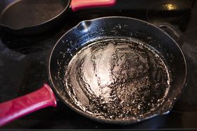 A used frying pan with a red handle on a stovetop traces of grease visible inside the pan